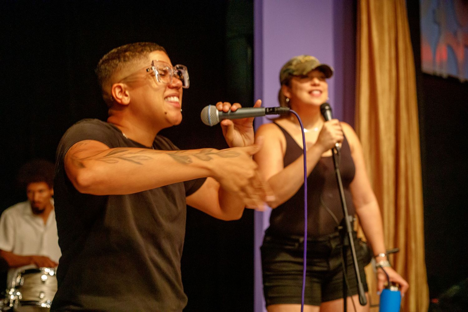 Two performers singing on stage with microphones under colorful stage lighting.