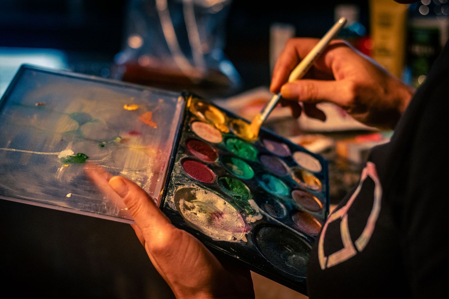 Close-up of hands holding a watercolor paint palette and brush during an art session.