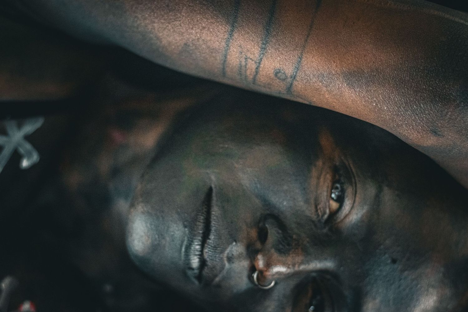 Dramatic close-up of a model with dark body paint and blue eyes lying down with painted markings on skin.