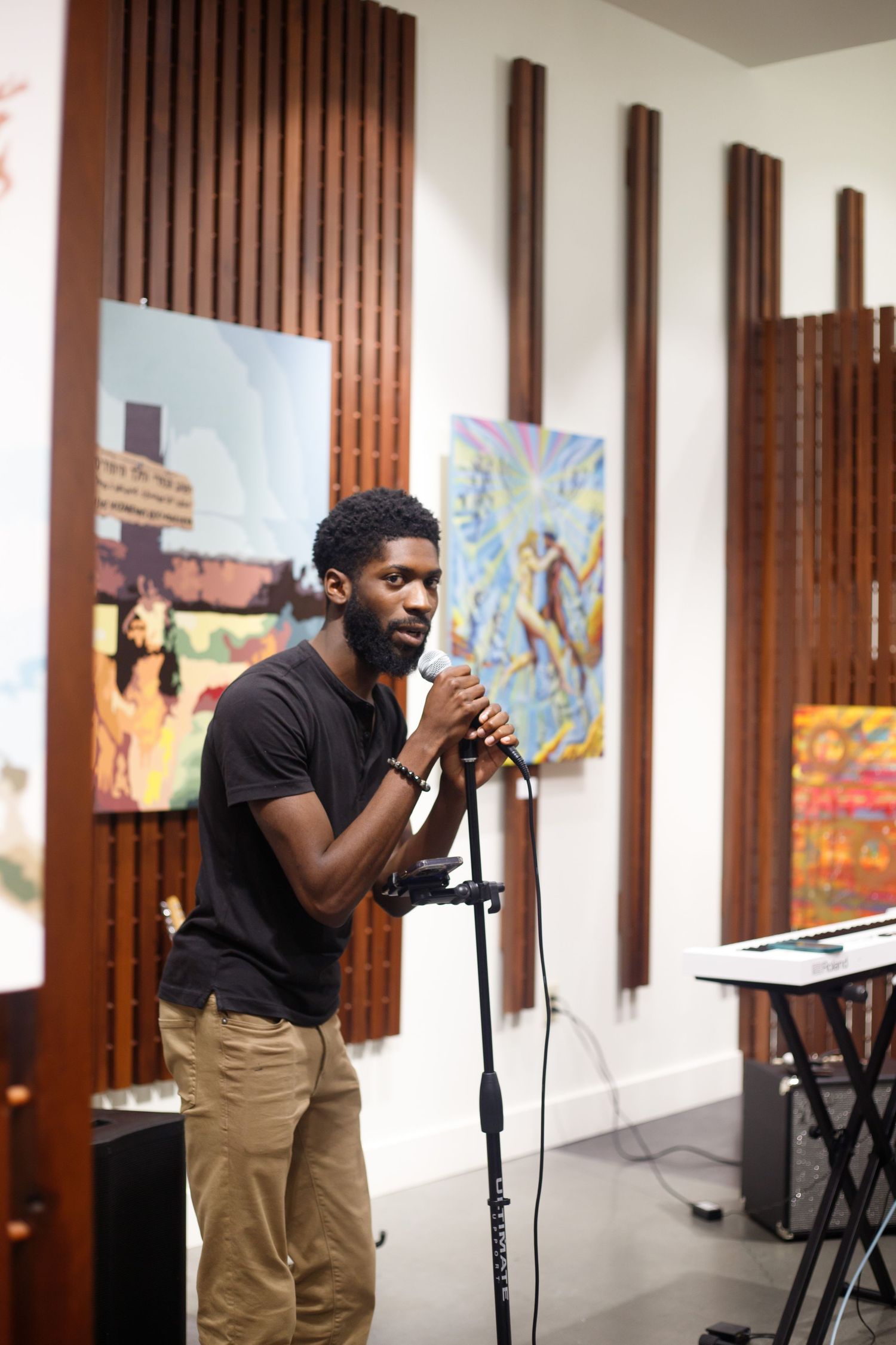 Man performing spoken word into a microphone at an art gallery with colorful paintings on the wall.