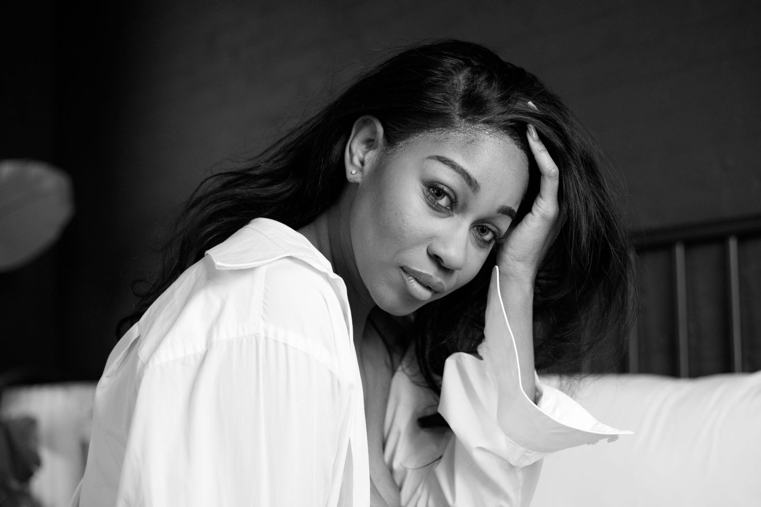 Black and white portrait of a pensive woman in a white shirt resting her head on her hand.
