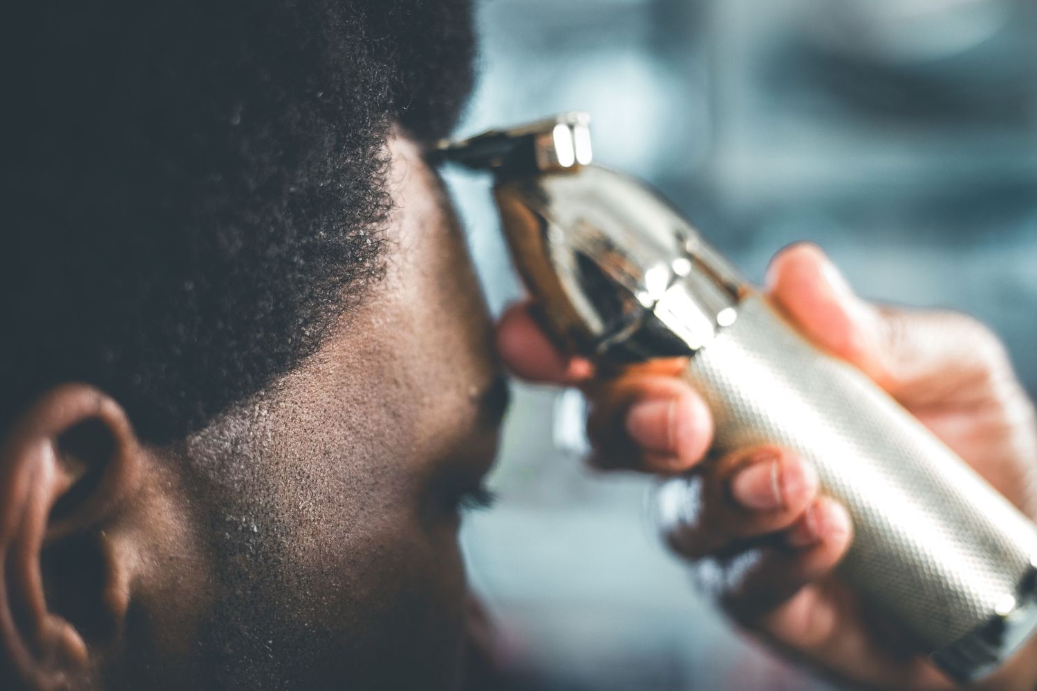 Close-up of a gold hair clipper being used near a man's face during a haircut.