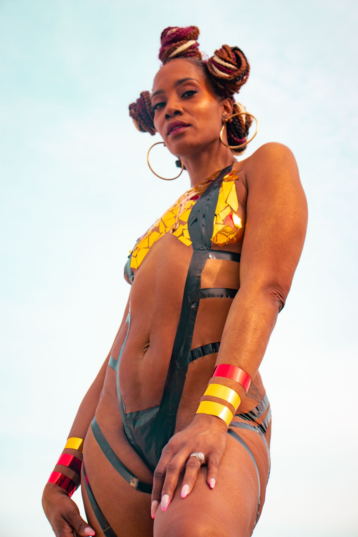 Woman in colorful African print bikini with red and yellow bangles posing against a blue sky.