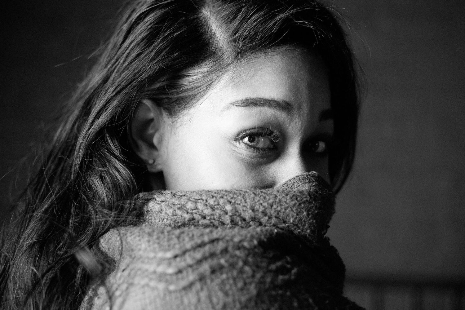 Black and white close-up of woman with dark hair hiding face in knit sweater.