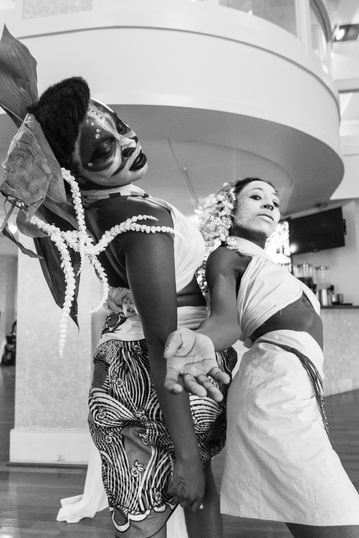 Black and white photo of two performers in traditional African costumes dancing together in an indoor venue.