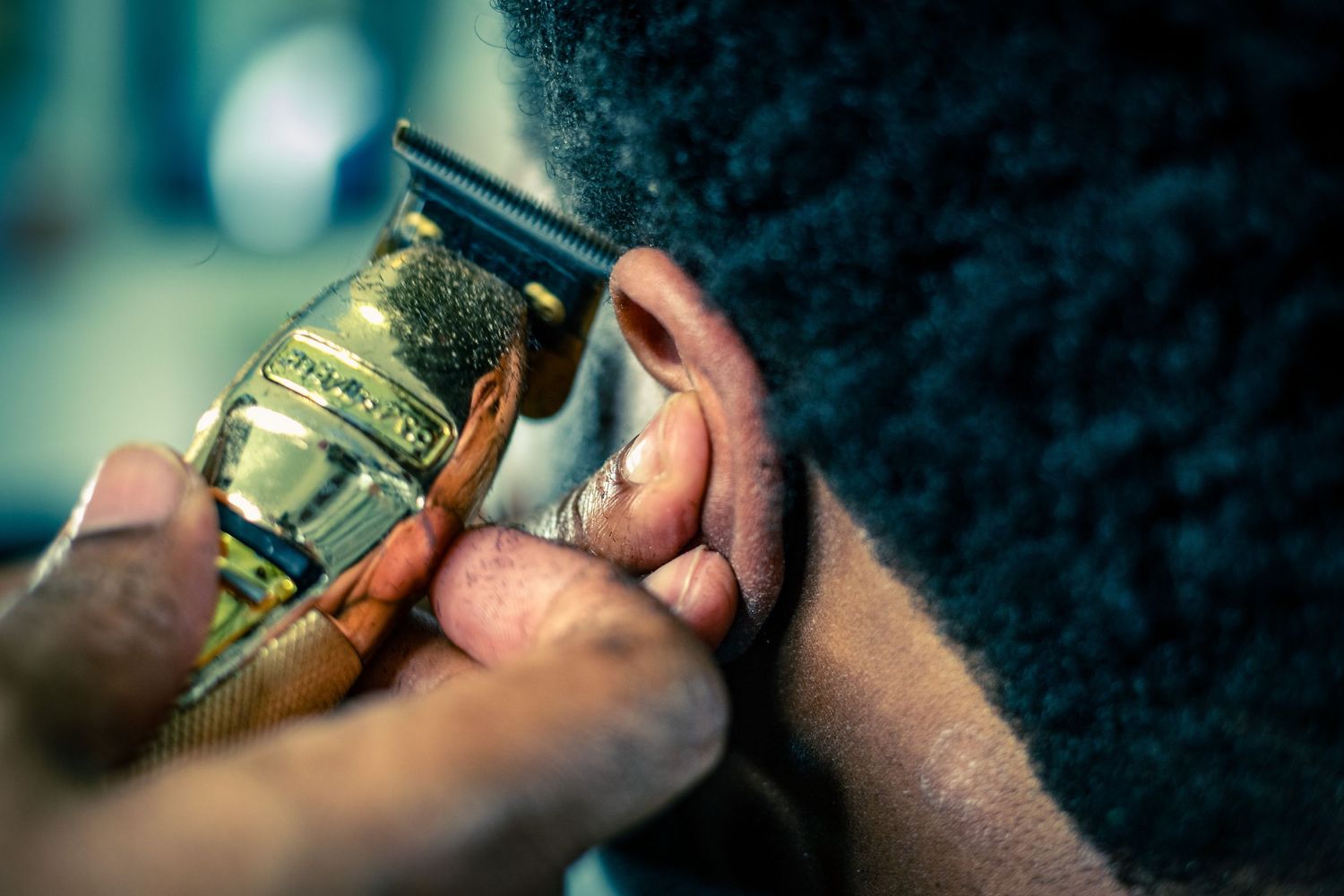 Extreme close-up of gold professional hair clippers trimming the side of a clients head.