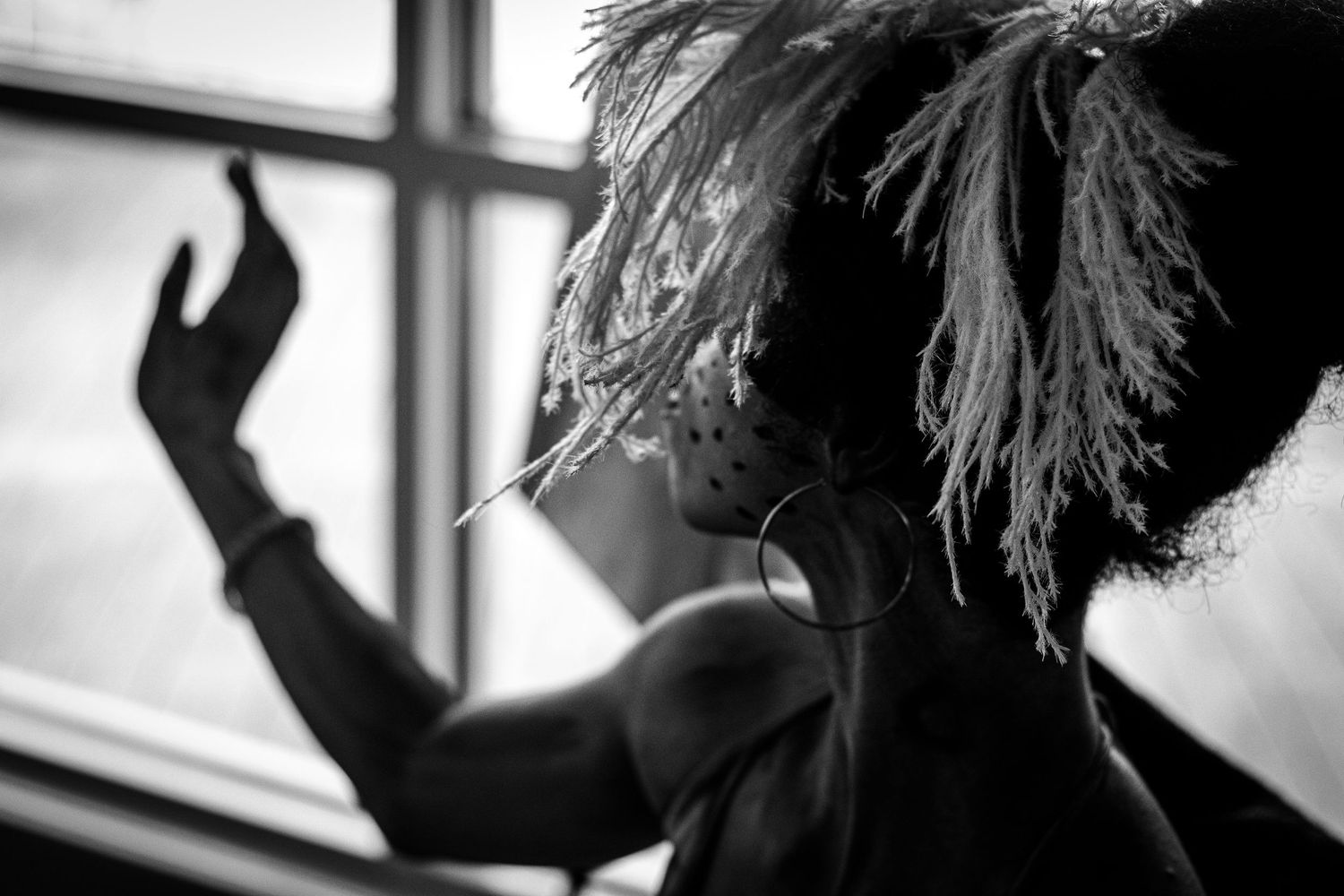 Black and white silhouette of a performer in feathered hat reaching toward a window with dramatic lighting.
