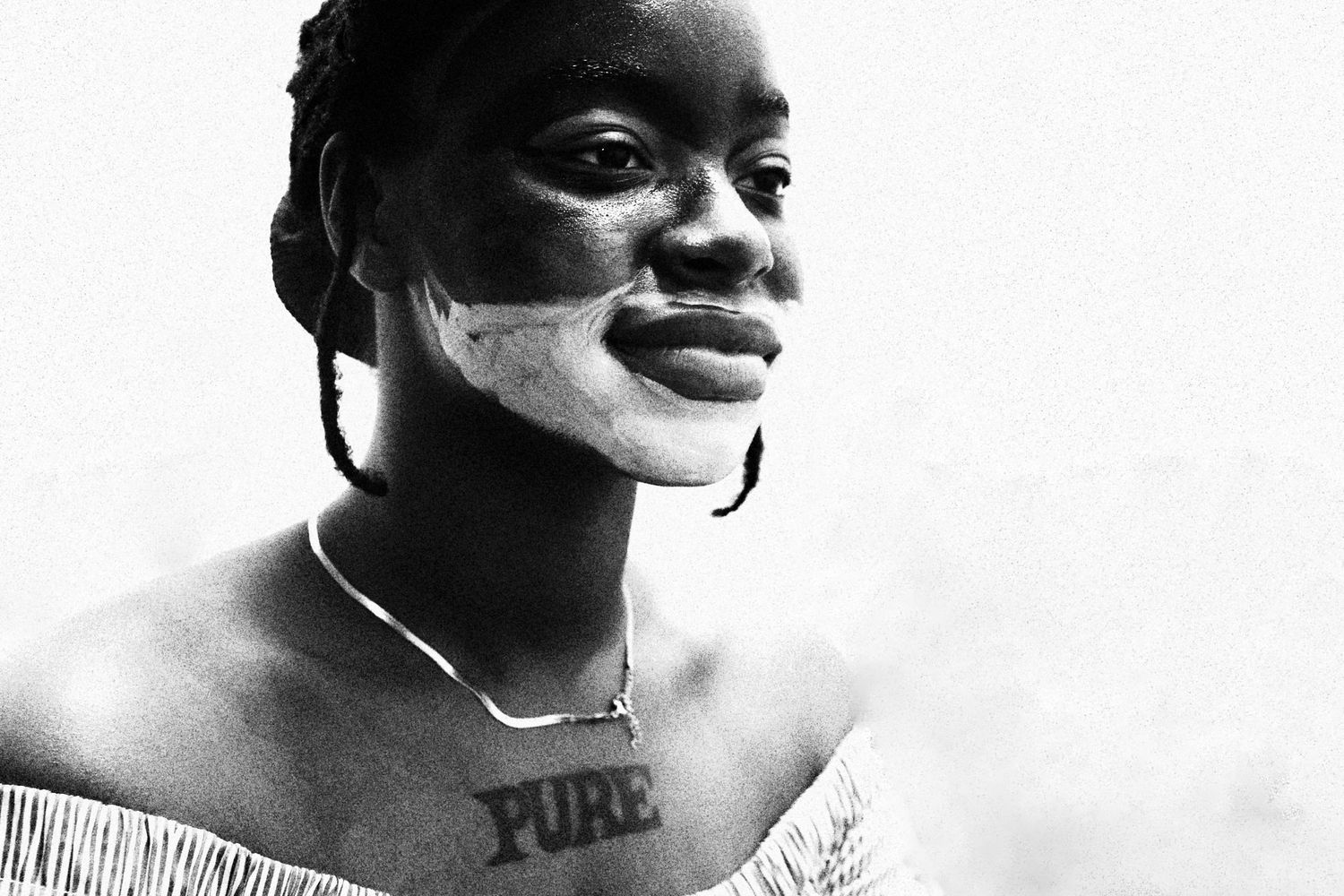 Black and white portrait of a young woman with face paint and a PURE tattoo on her chest.