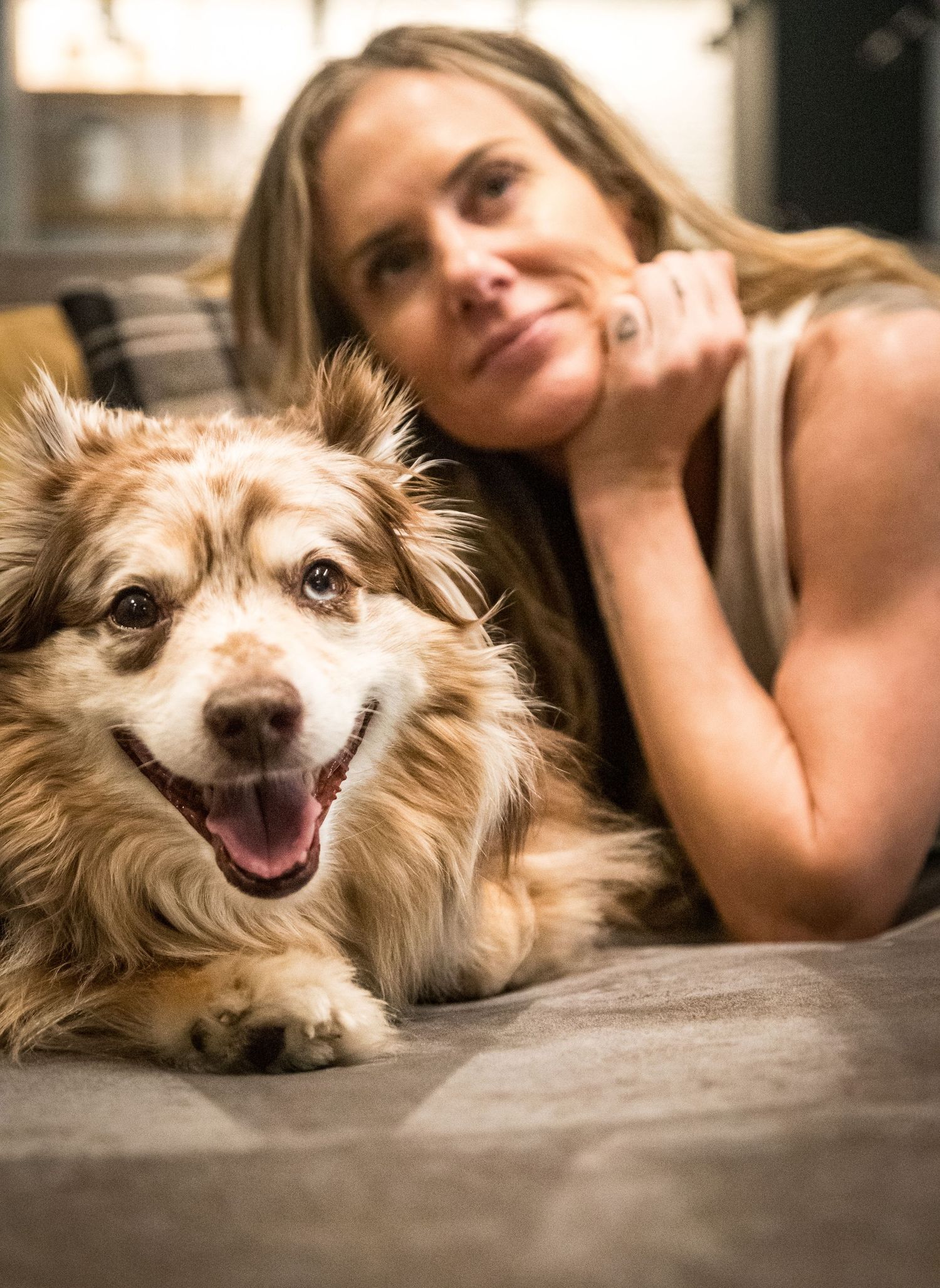 Woman resting her head near her happy fluffy brown and white dog on a bed.