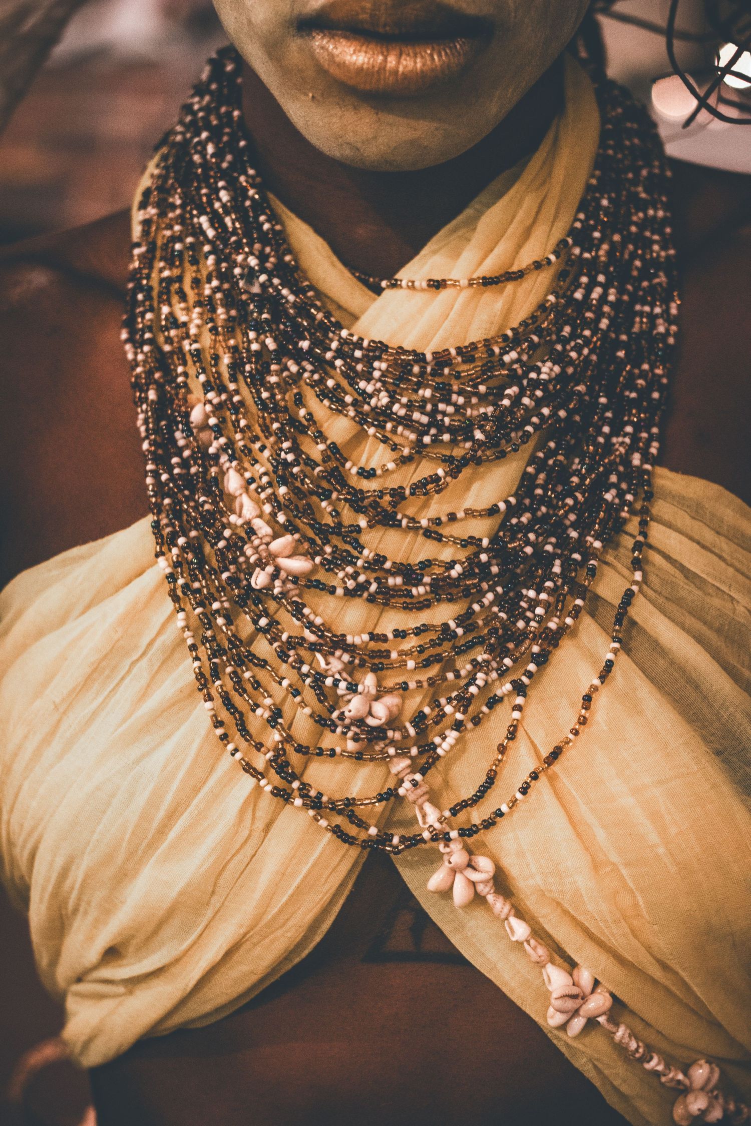 Close-up of layered beaded necklaces with shell accents worn over a cream fabric garment.