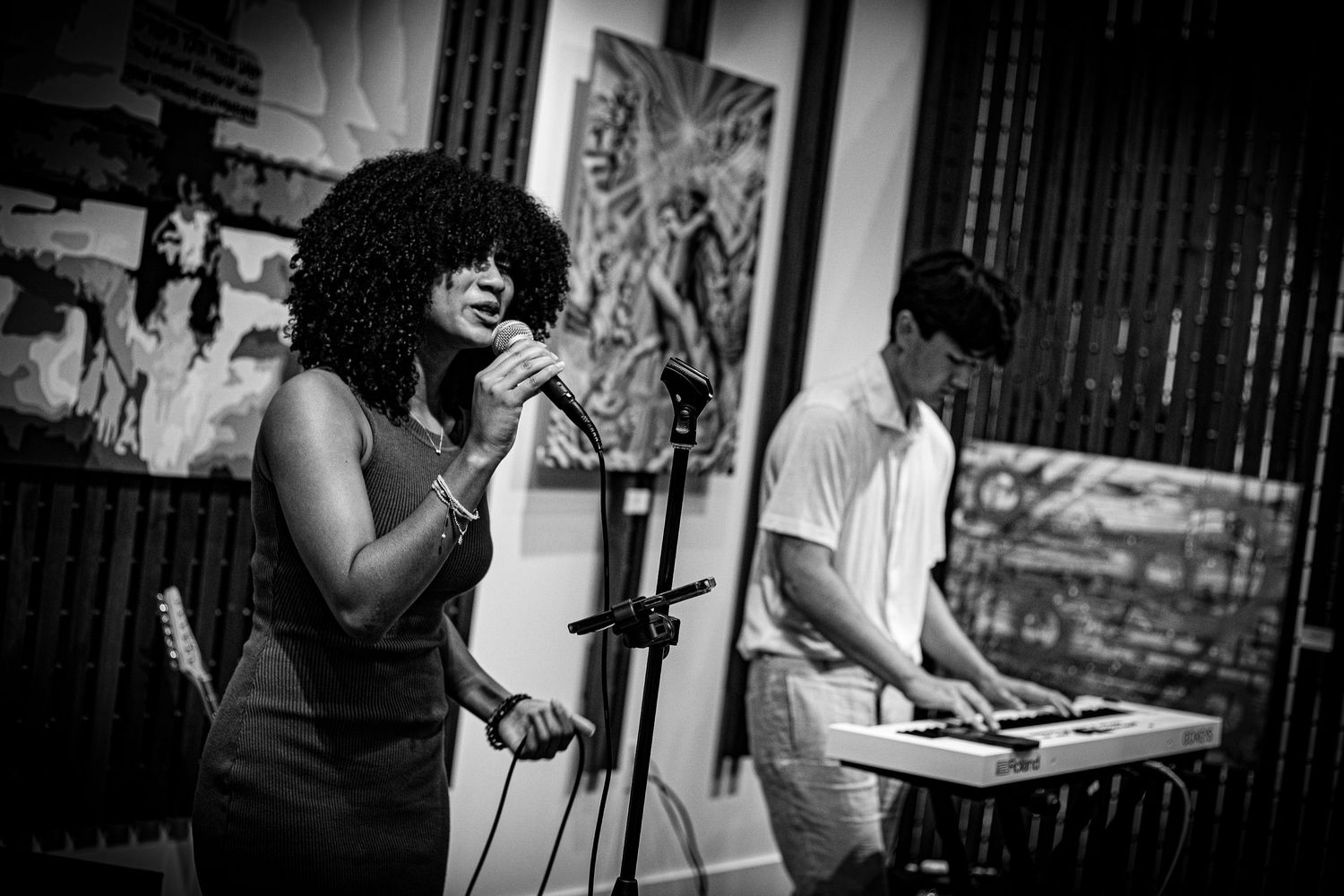 Black and white photo of female singer performing with keyboard musician in gallery.