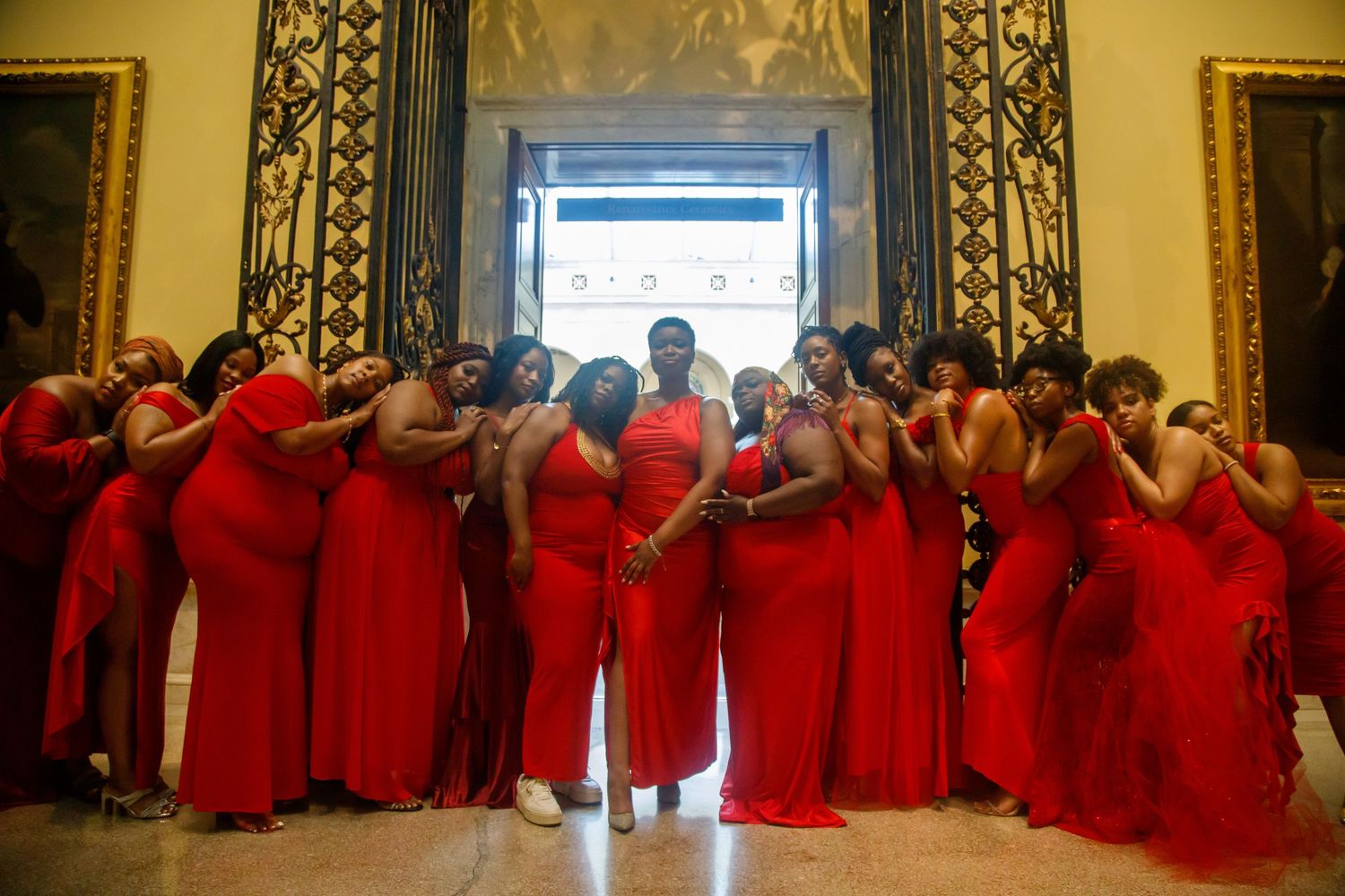 Large group of women in red dresses posing in grand hall.