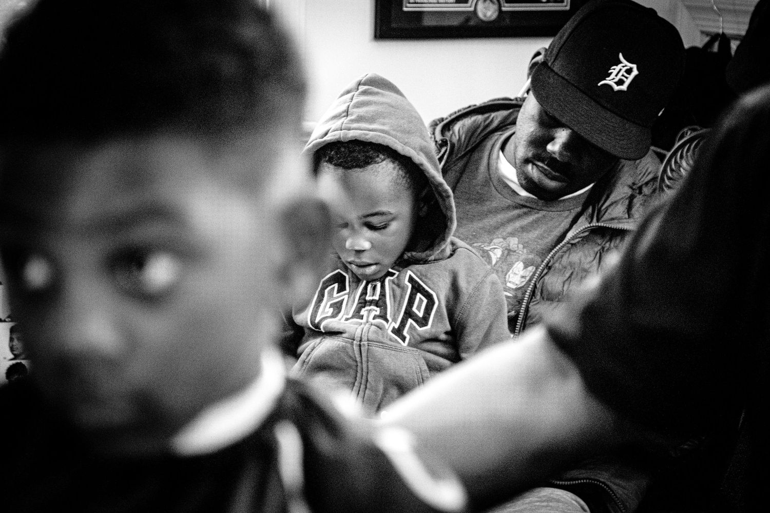Black and white photo of a father holding his child while waiting in a barbershop.