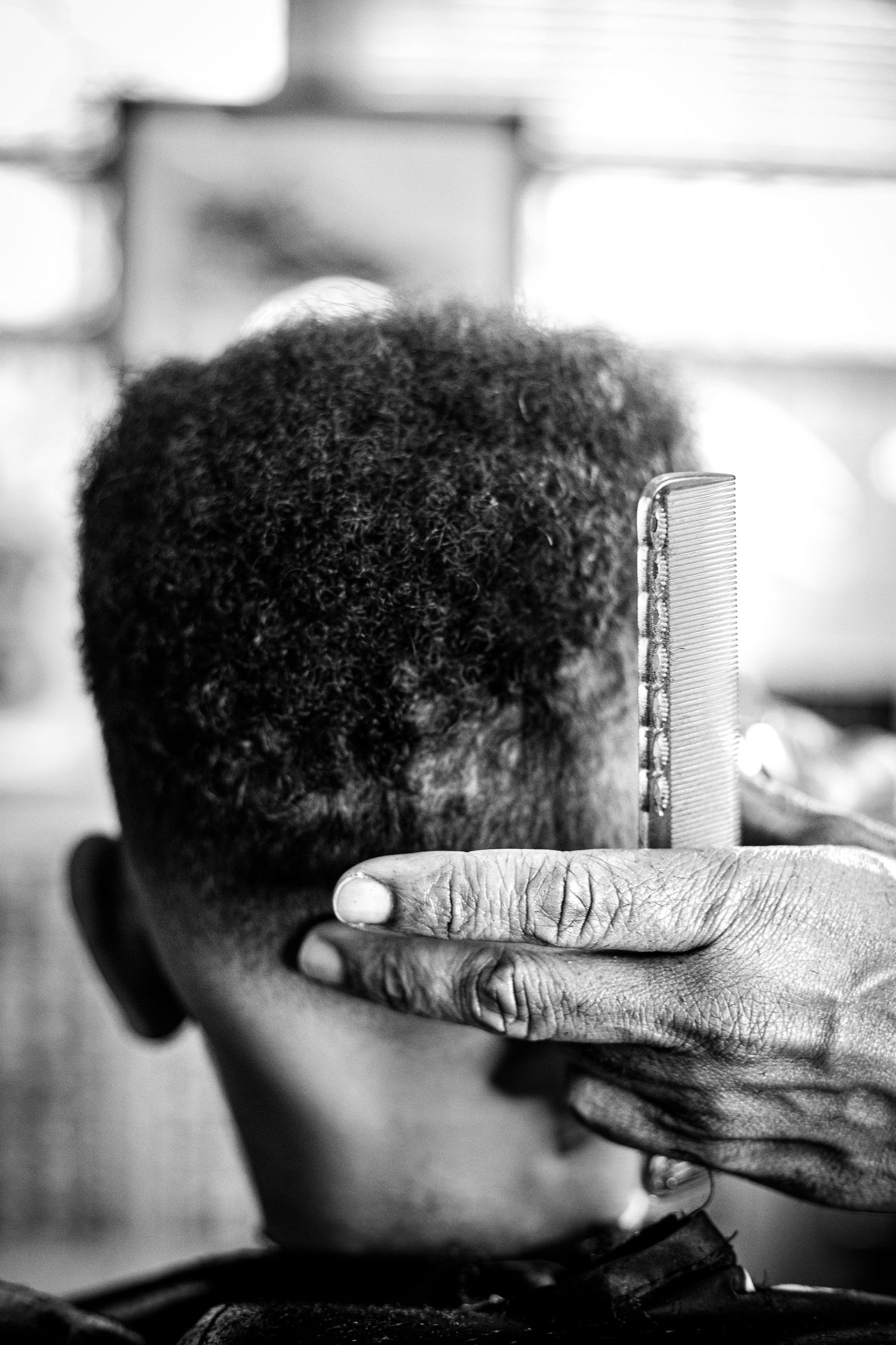 Black and white close-up of a barber's hand holding a comb against a client's curly hair.