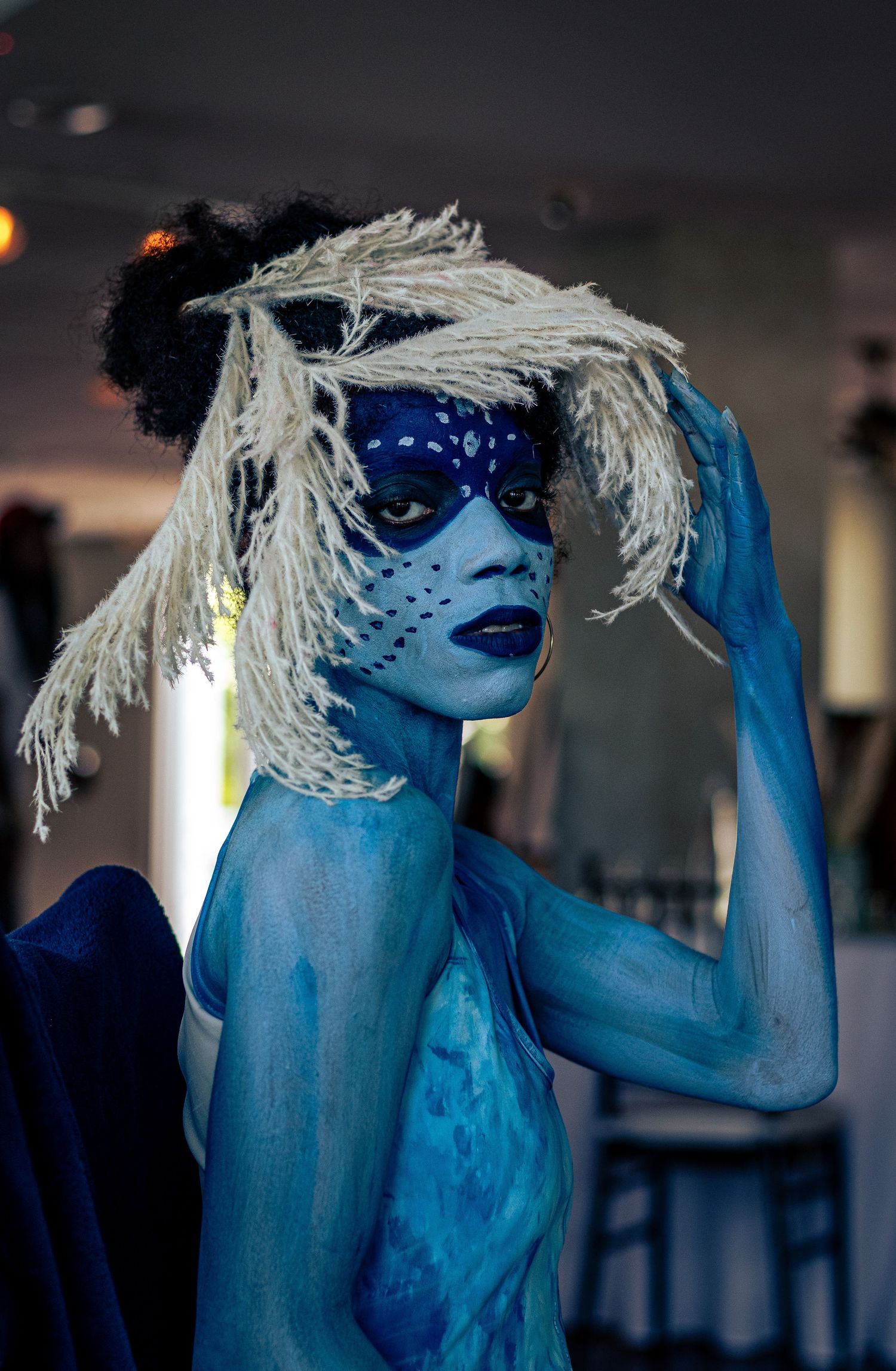 Model with full blue body paint and white wig poses dramatically in an artistic performance look.