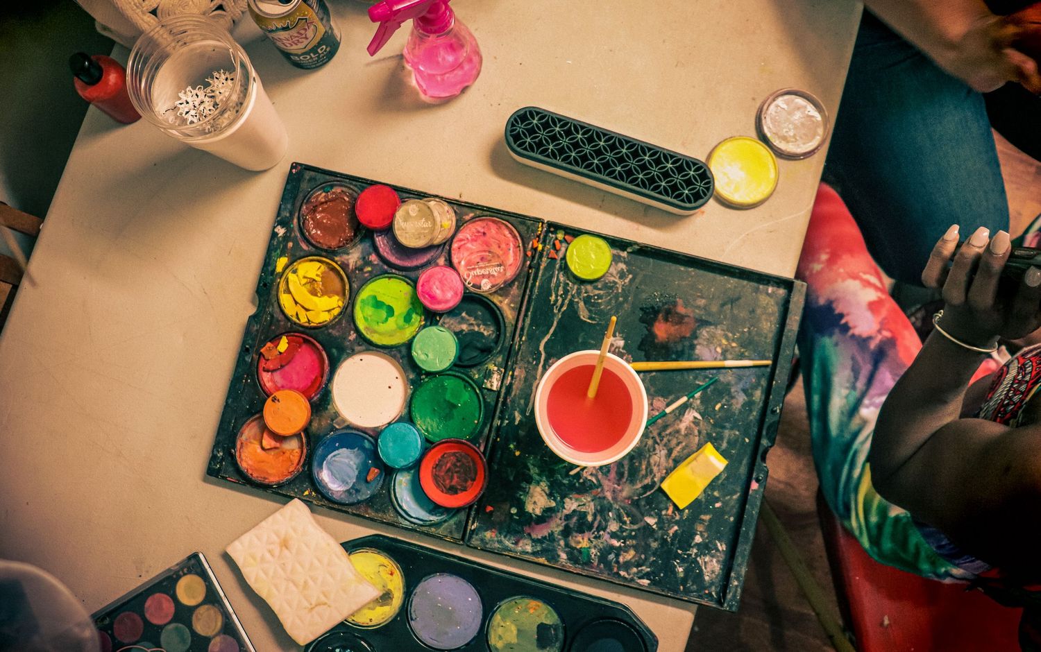 Colorful paint palette with brushes and art supplies on a messy table during a creative painting session.