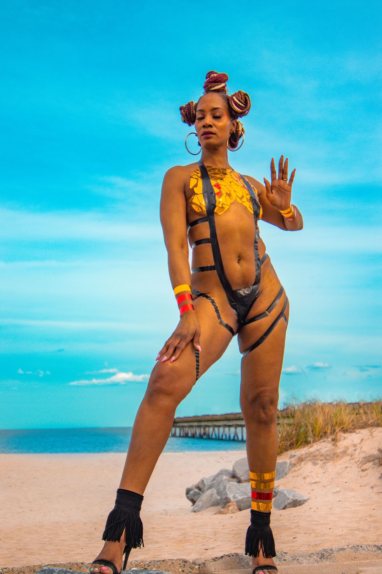 Woman in colorful strappy festival swimsuit posing on sandy beach with blue sky backdrop.