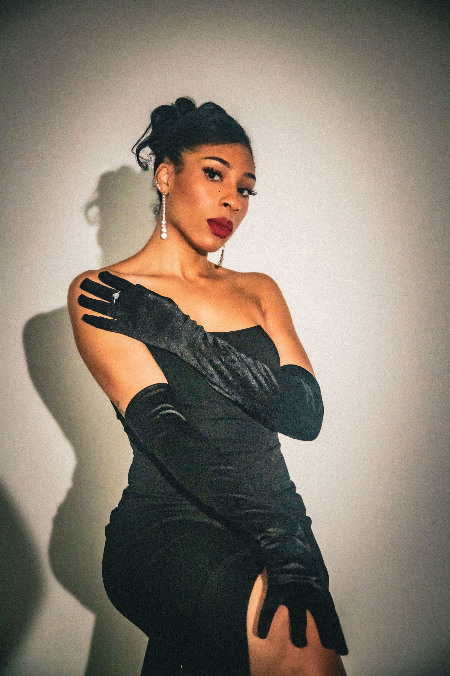 Glamorous woman in black strapless gown and long satin gloves posing gracefully against a white wall.