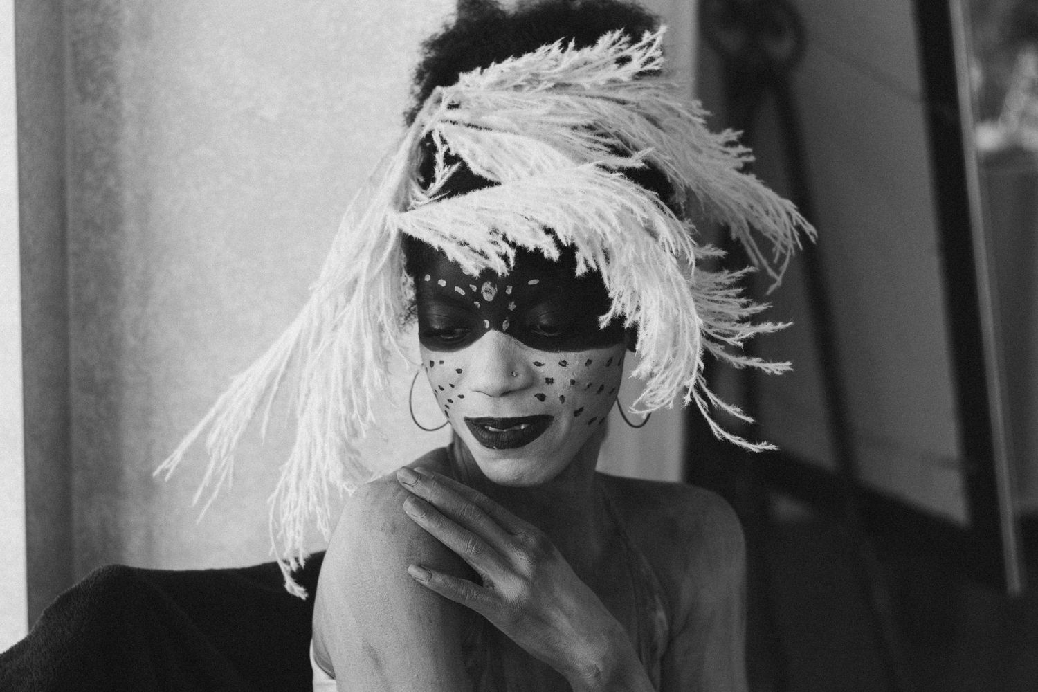 Black and white photo of a performer wearing a feathered masquerade mask with polka dots and white plumes.