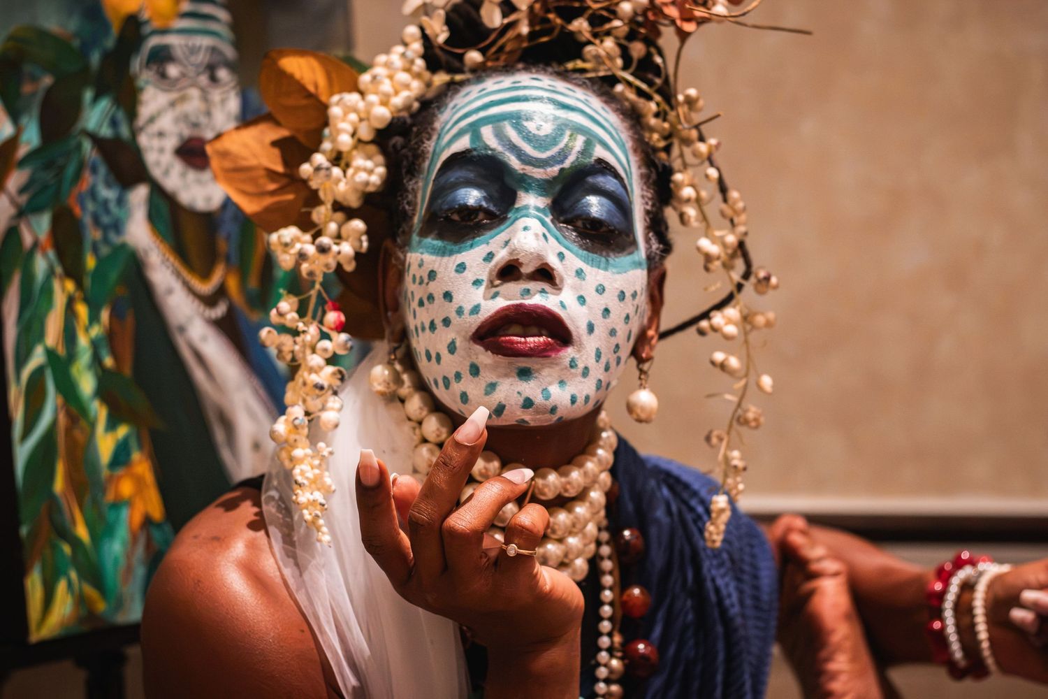 Performer with white dotted blue face paint and floral crown blowing a kiss to camera.