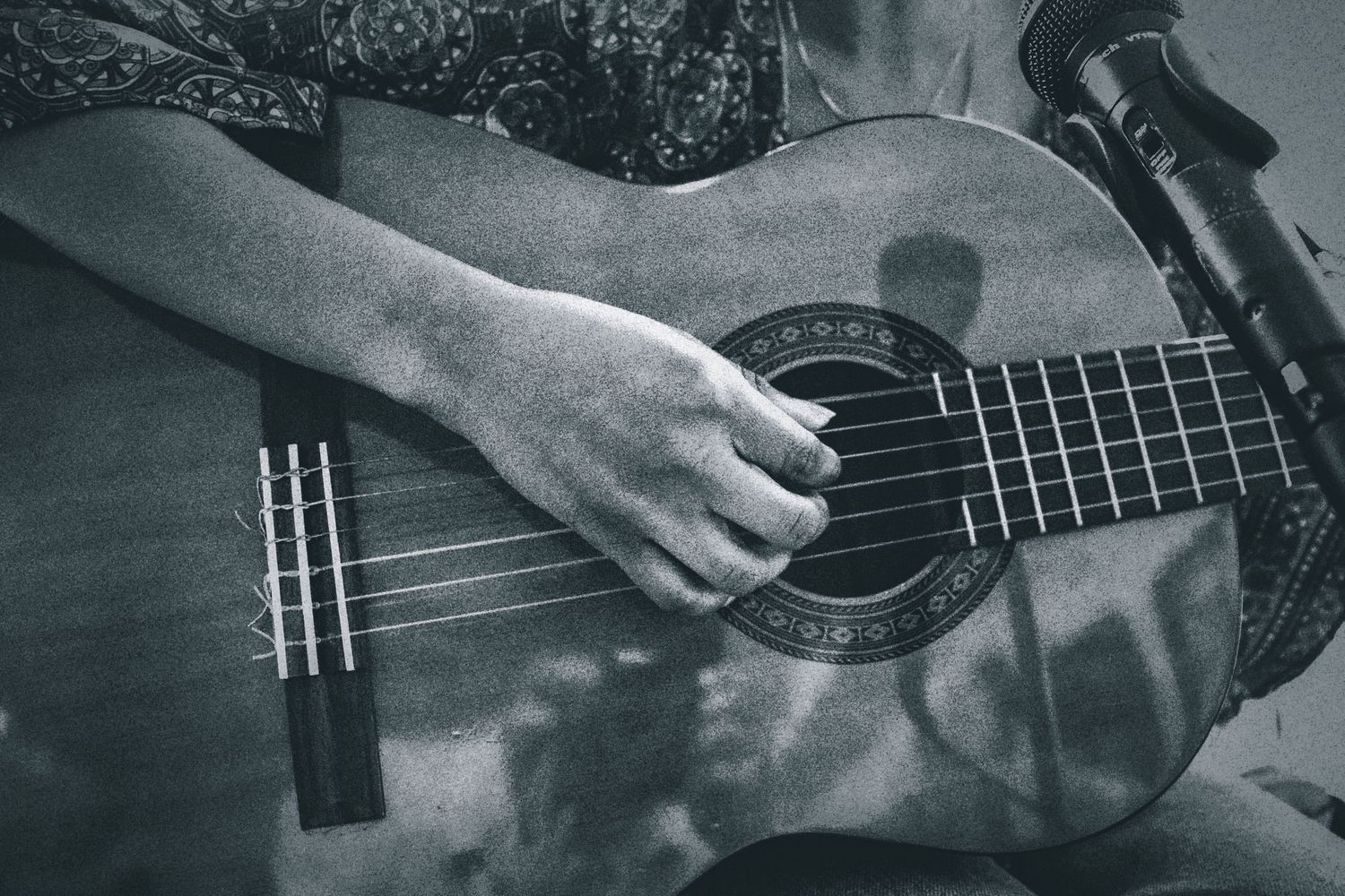 Close-up black and white photo of hands strumming an acoustic guitar near a microphone.