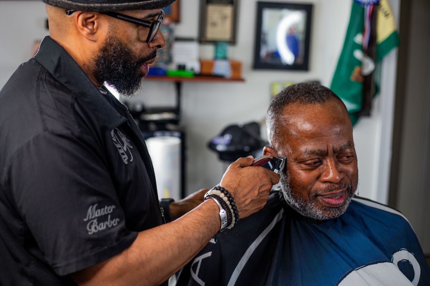 A master barber carefully trims the ear area of an older man in a professional barbershop.