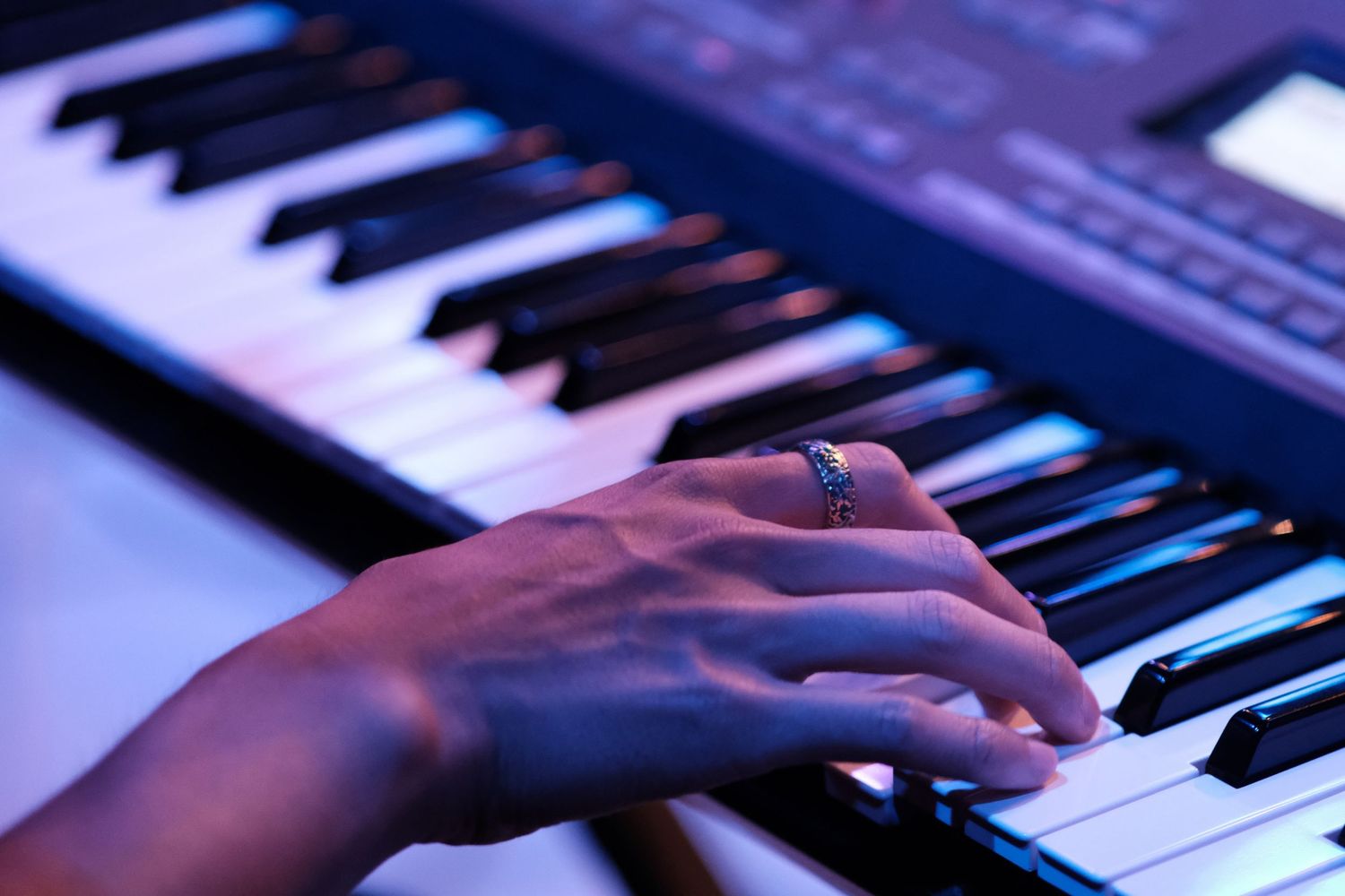 Close-up of hand wearing ring playing colorful illuminated electronic keyboard.