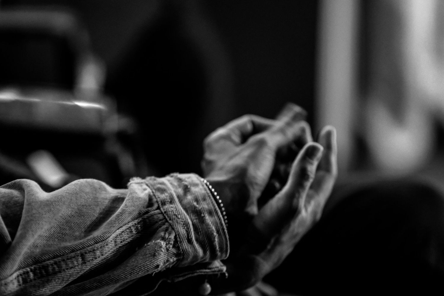 Black and white close-up of elderly hands clasped together wearing denim jacket.