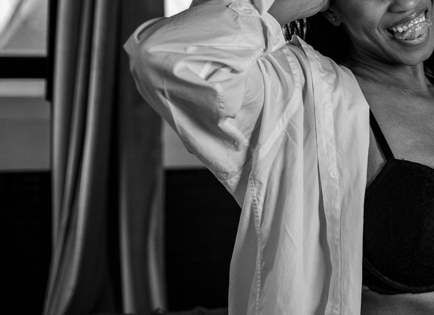 Black and white photo of a smiling woman in a bra adjusting her white shirt.