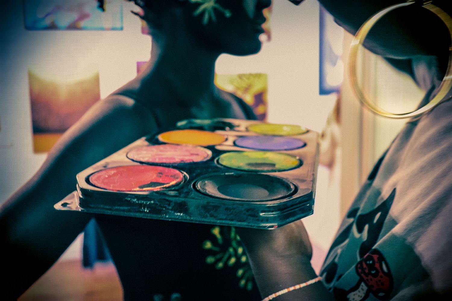 Close-up of a vibrant paint palette with colorful pigments held by a person wearing gold hoop earrings.