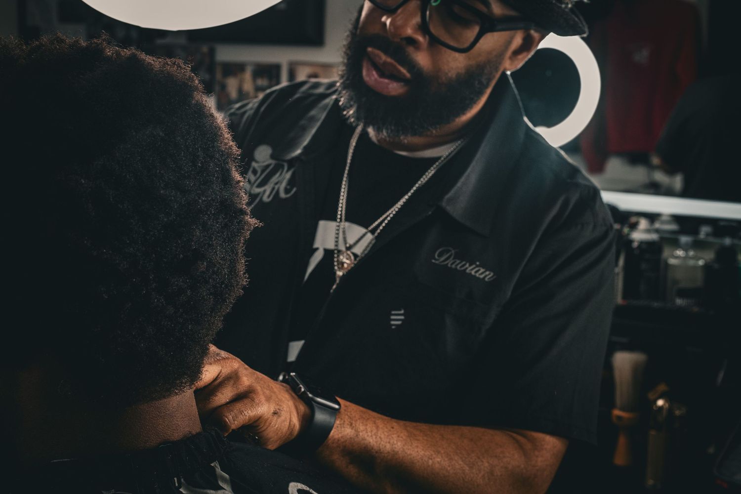 Barber carefully detailing a clients natural hair in a dimly lit professional barbershop.