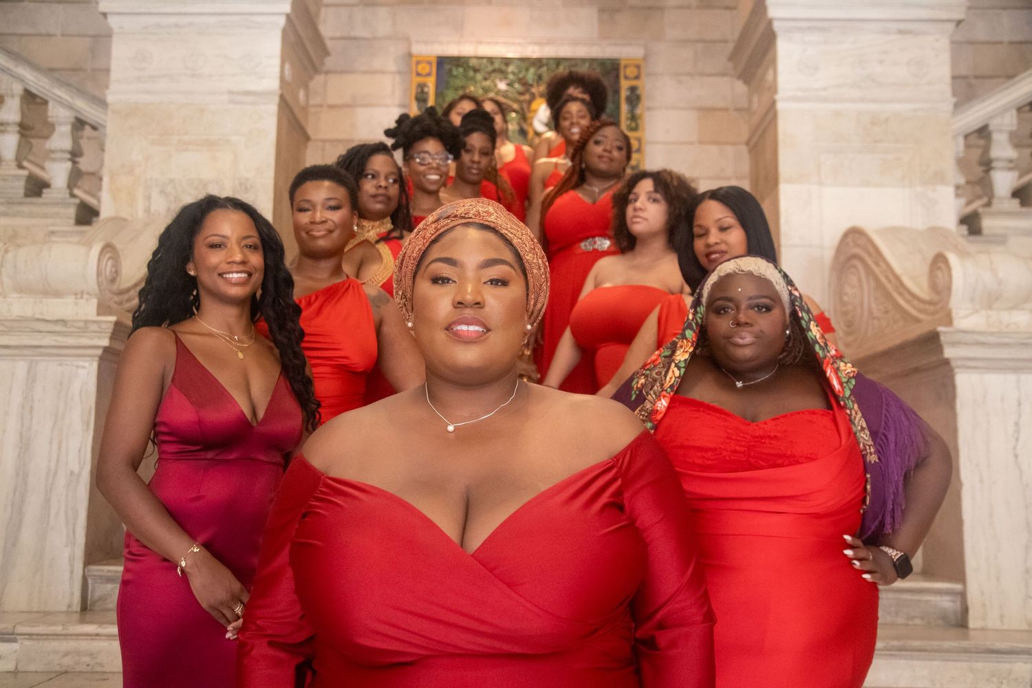 Group of women in red dresses posing on grand staircase for elegant formal photo.
