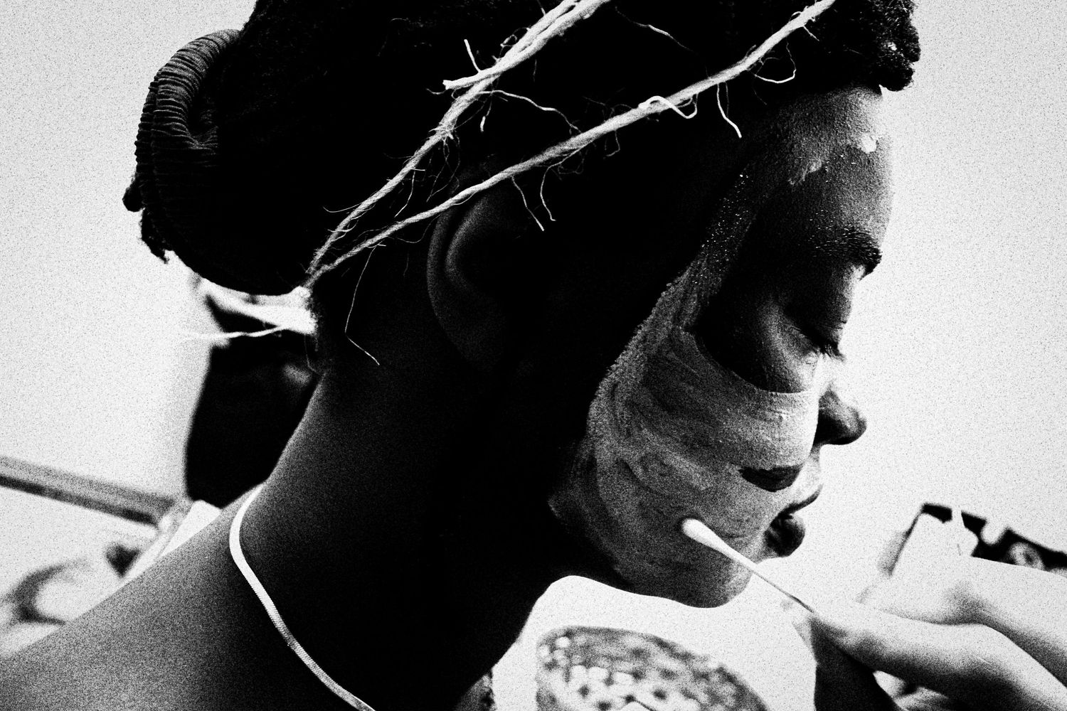 Black and white portrait of a person with white face paint and braided hair during a body art session.