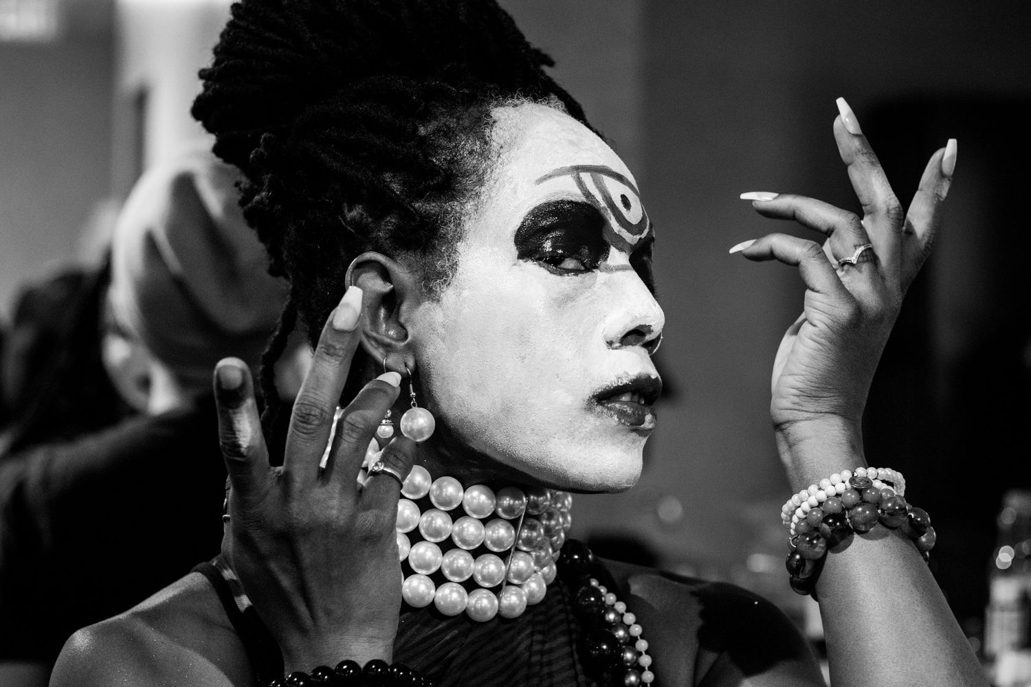 Black and white portrait of woman with dramatic white face paint and bold eye makeup applying cosmetics.