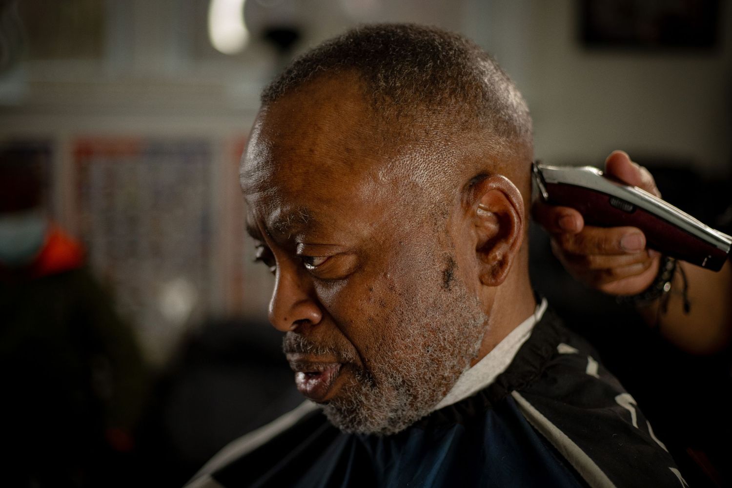 Close-up of an elderly Black man receiving a haircut with electric clippers in a barbershop.