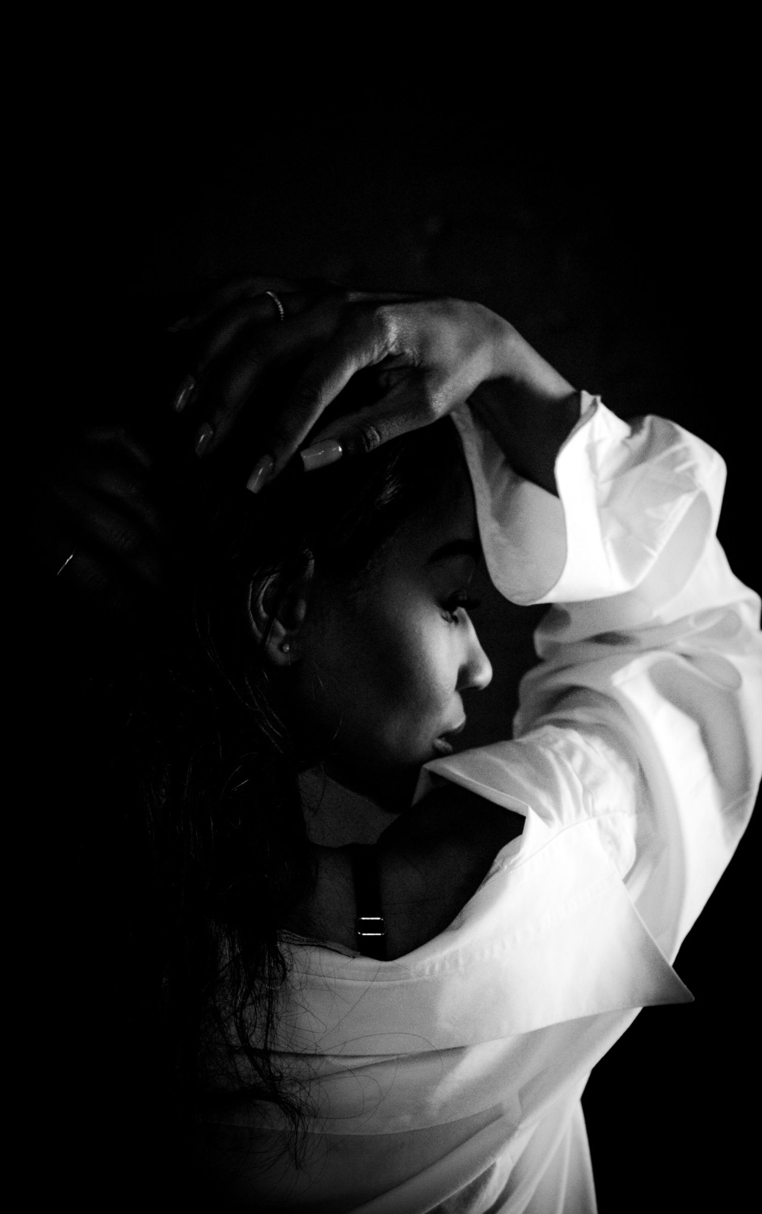 Dramatic black and white portrait of a woman in white shirt against dark background.