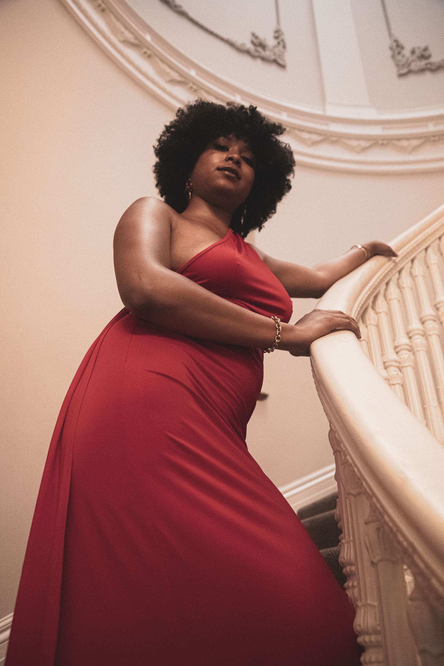 Low angle view of woman in red halter dress posing gracefully on ornate white staircase.