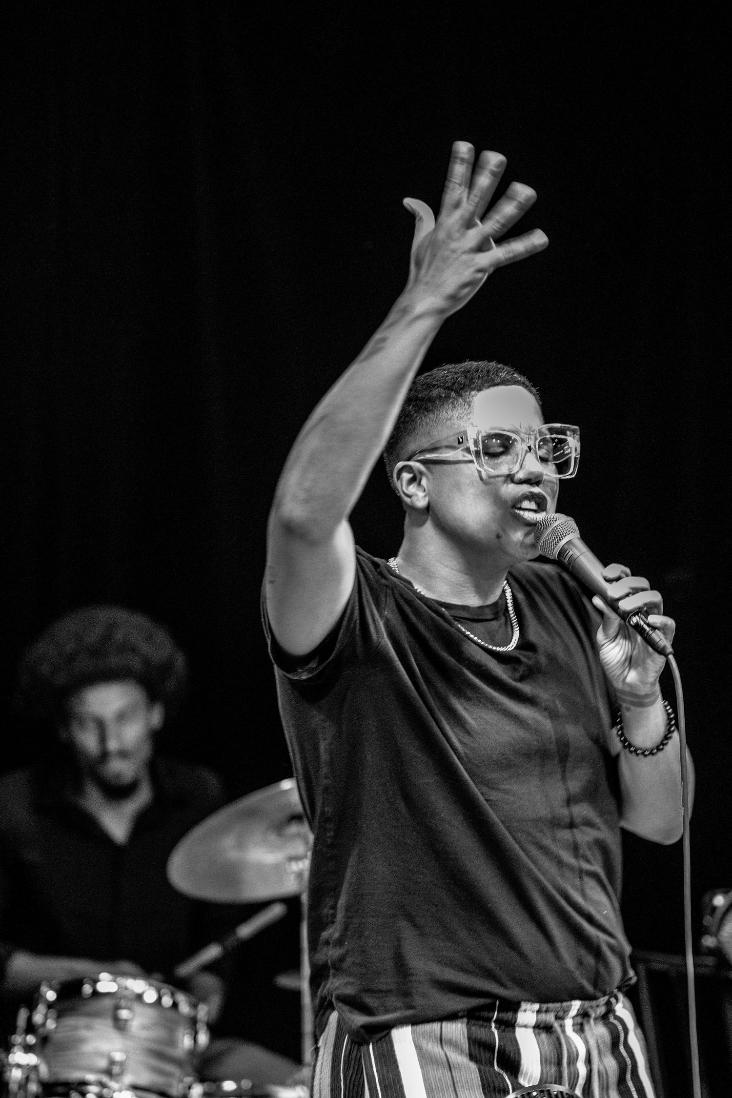 Black and white photo of a performer singing on stage with hand raised.