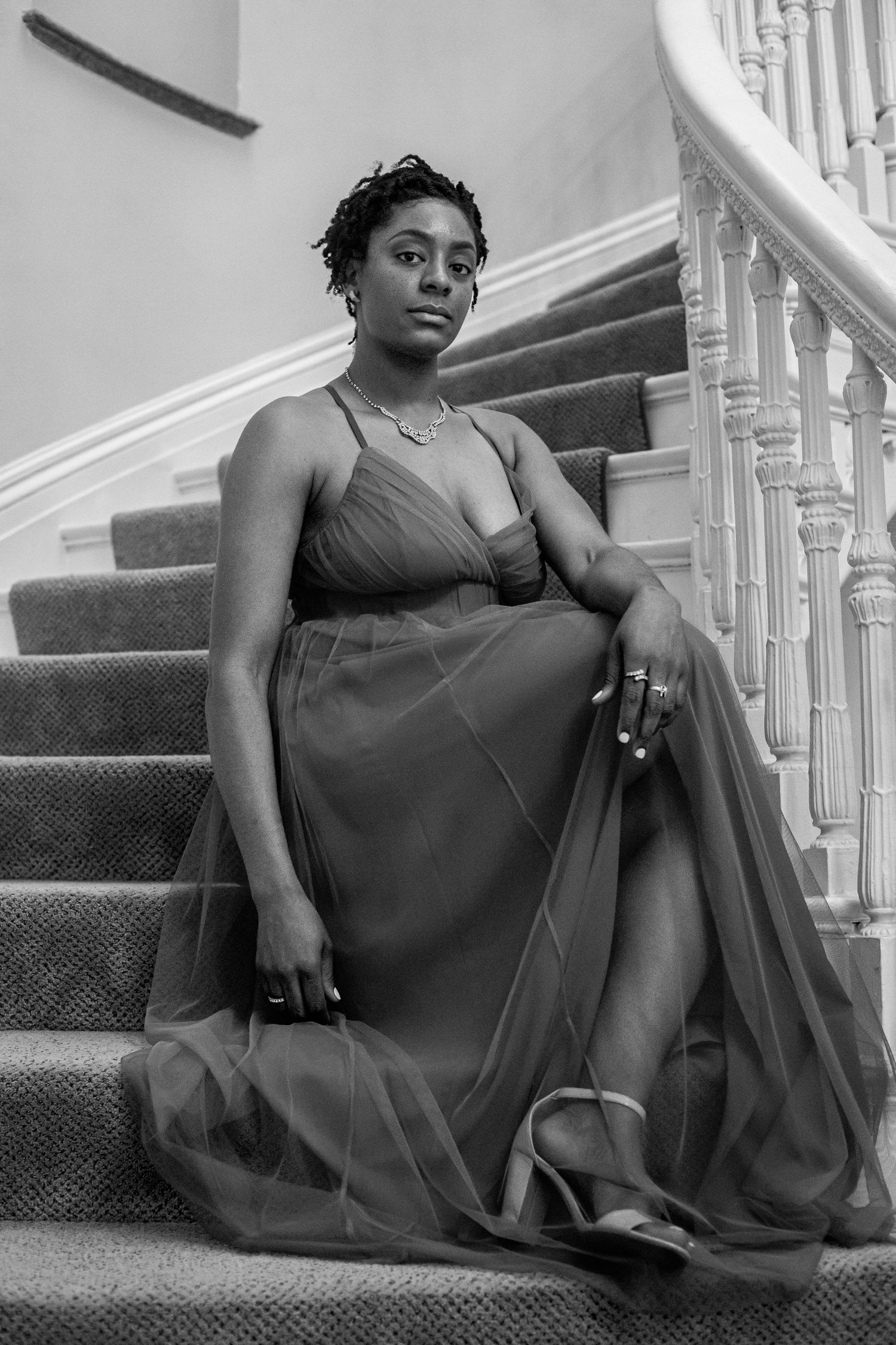 Woman in flowing gown sitting gracefully on staircase in black and white portrait.