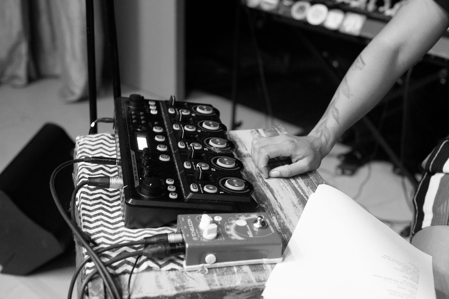 Close-up black and white photo of a musician using an electronic music controller and mixing equipment on stage.