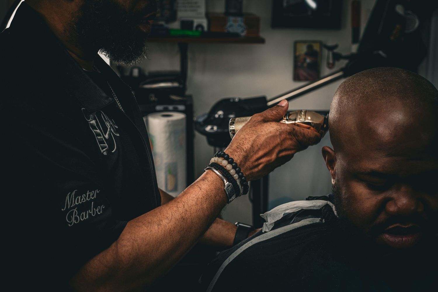 A master barber carefully uses clippers on a clients head in a dimly lit barbershop.