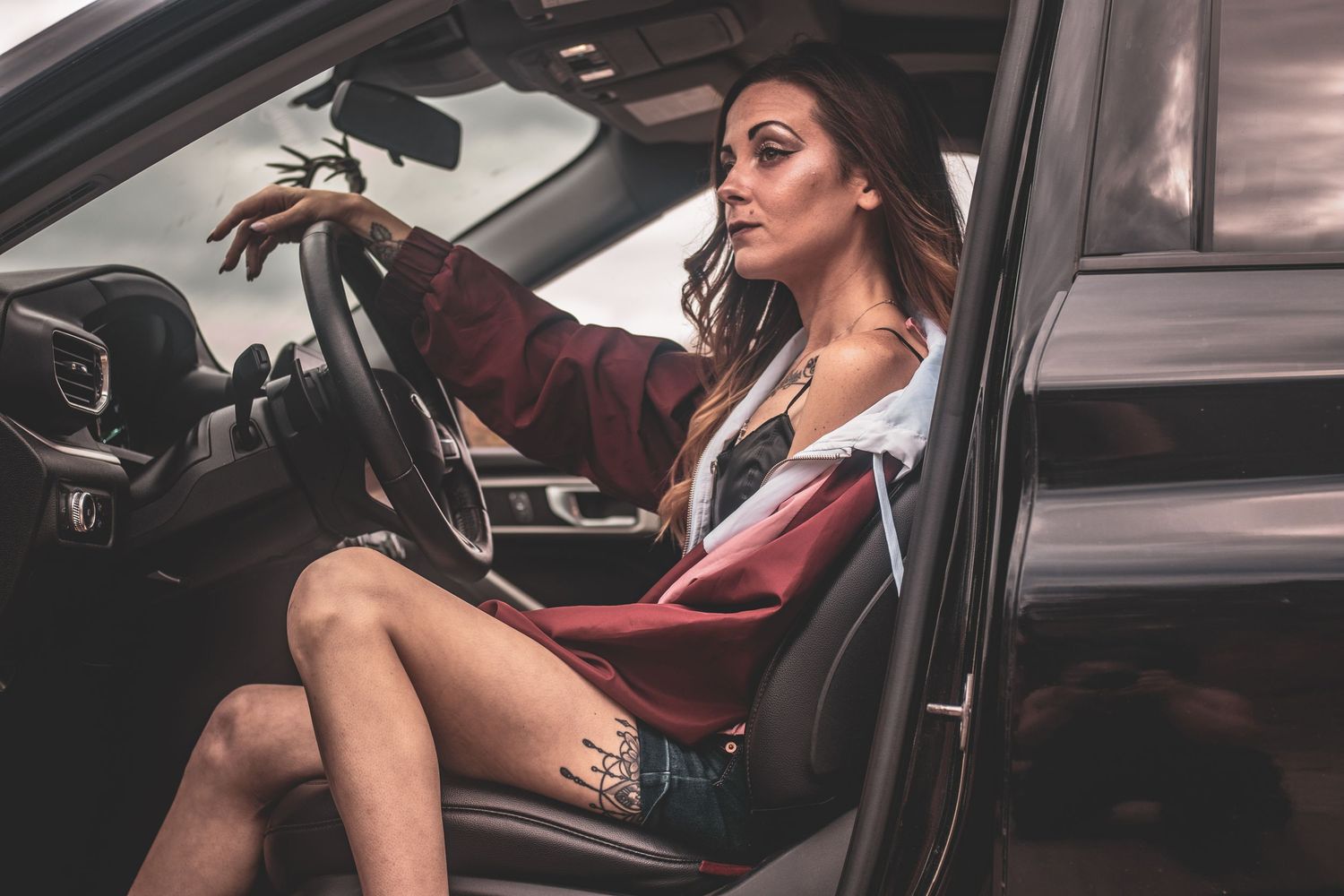 Stylish woman in denim shorts and blazer sitting in a car holding the steering wheel.