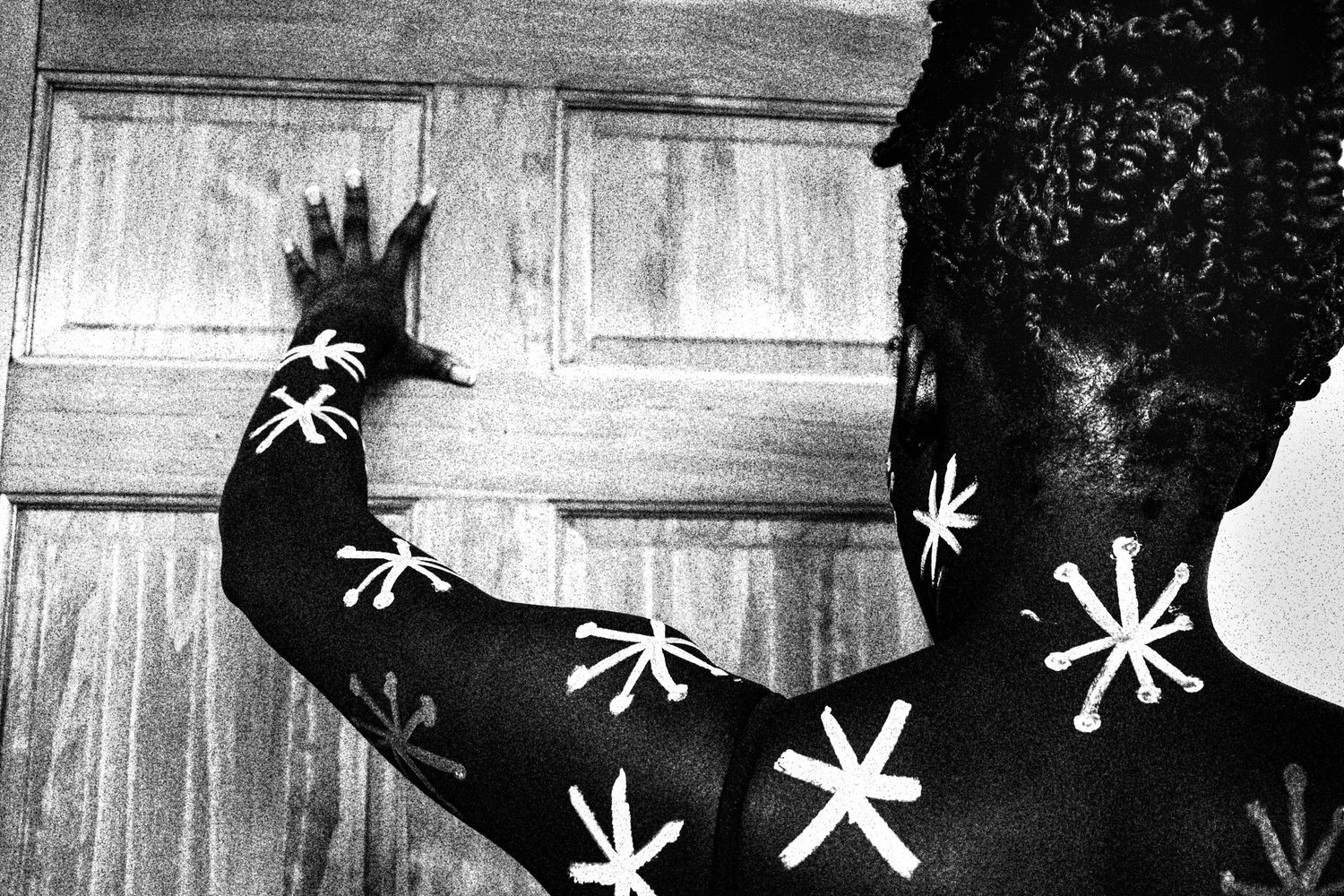 Black and white photo of a person with white star patterns painted on their dark body-painted back.