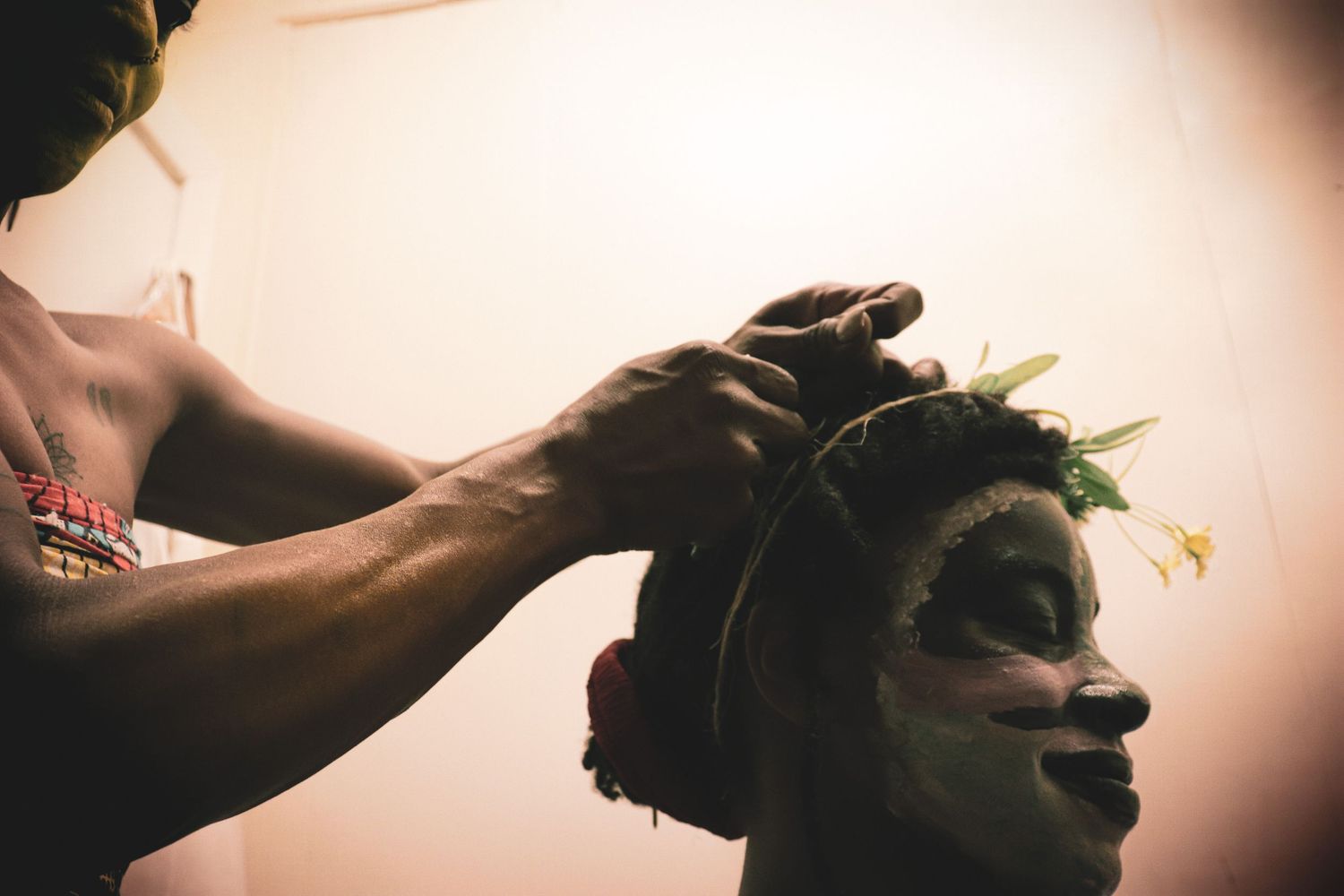Artist carefully placing green foliage on a model wearing green face paint in warm light.