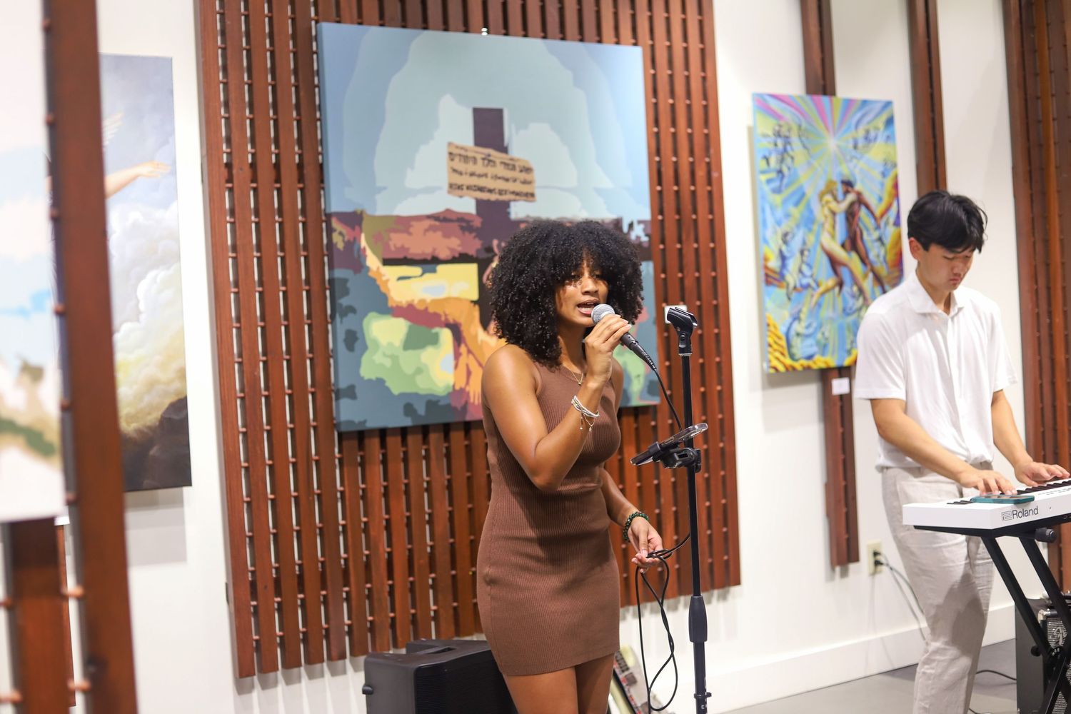 Female singer performing at microphone in art gallery with keyboard player accompanist.