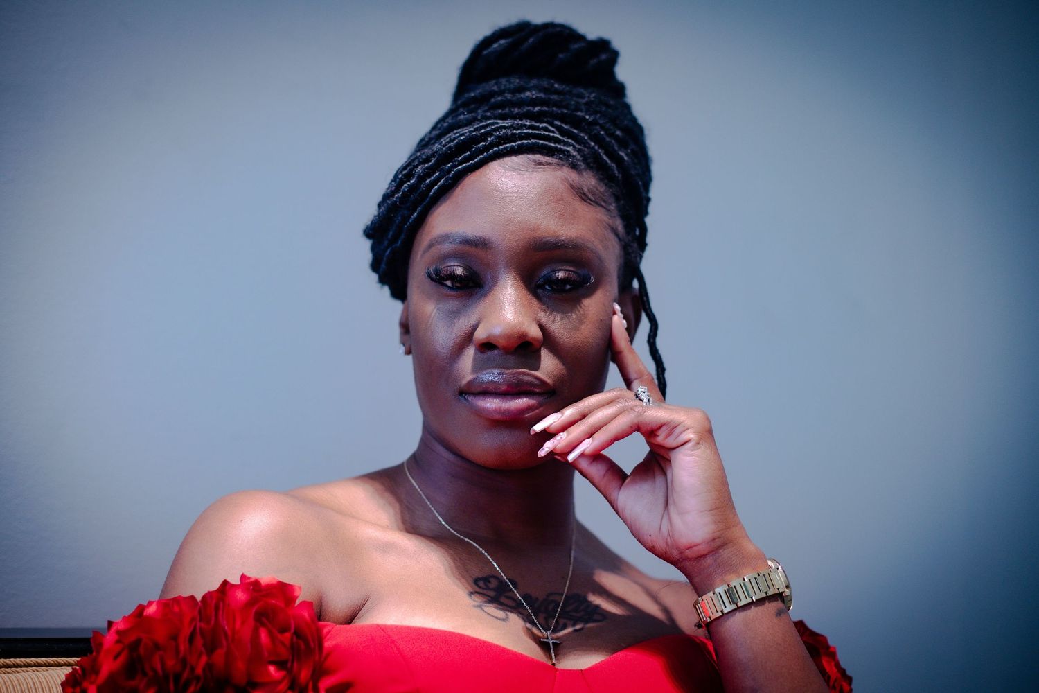 Close-up portrait of a Black woman in a red strapless dress with braided updo and red floral accessory.