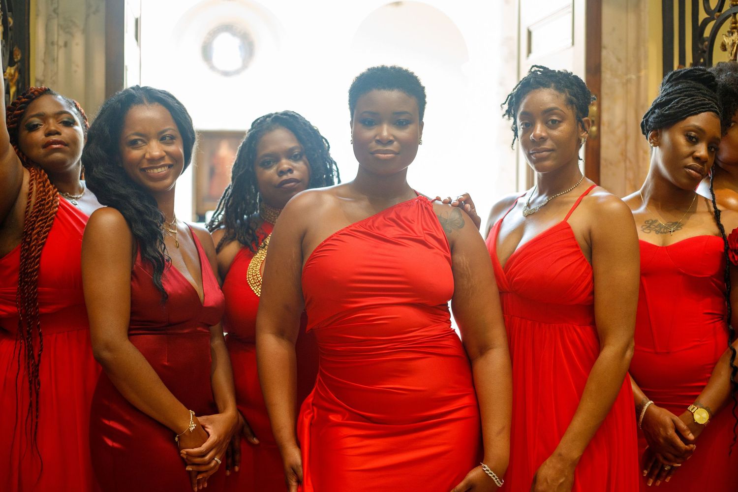 Group of women in red dresses posing in elegant interior.