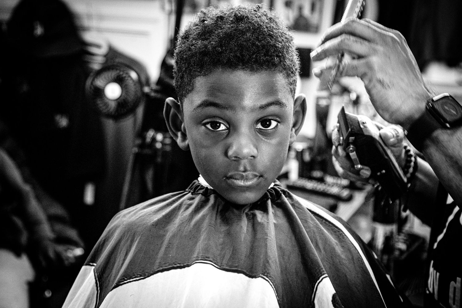 Black and white portrait of a young boy getting a haircut in a barbershop.