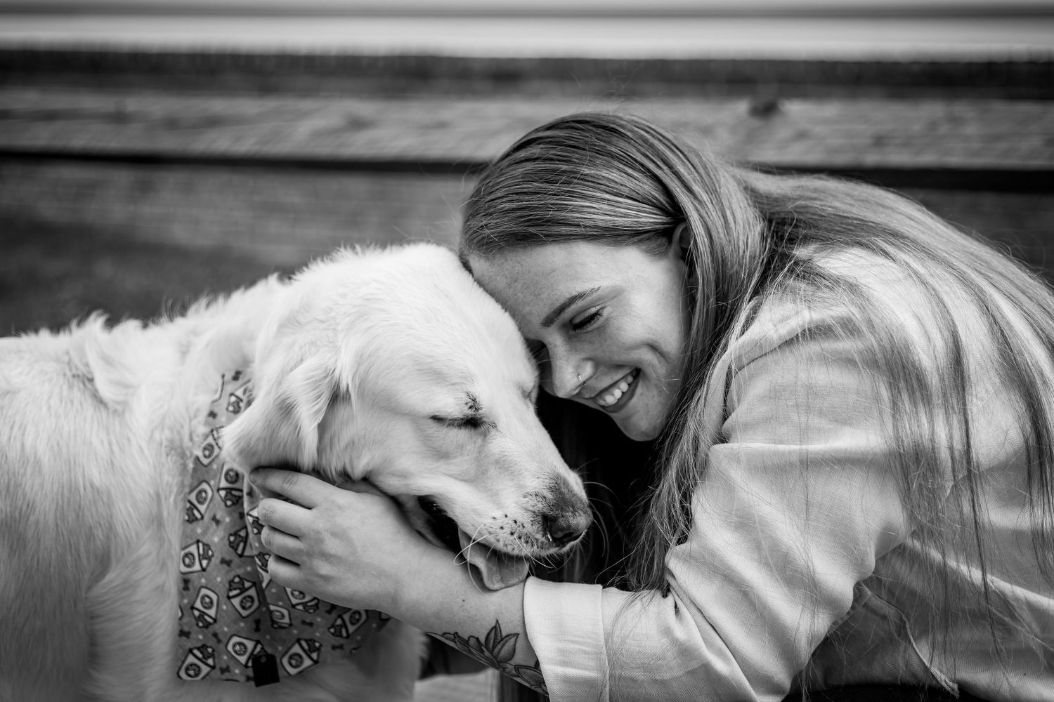 Black and white photo of a woman smiling and hugging a golden retriever dog affectionately.