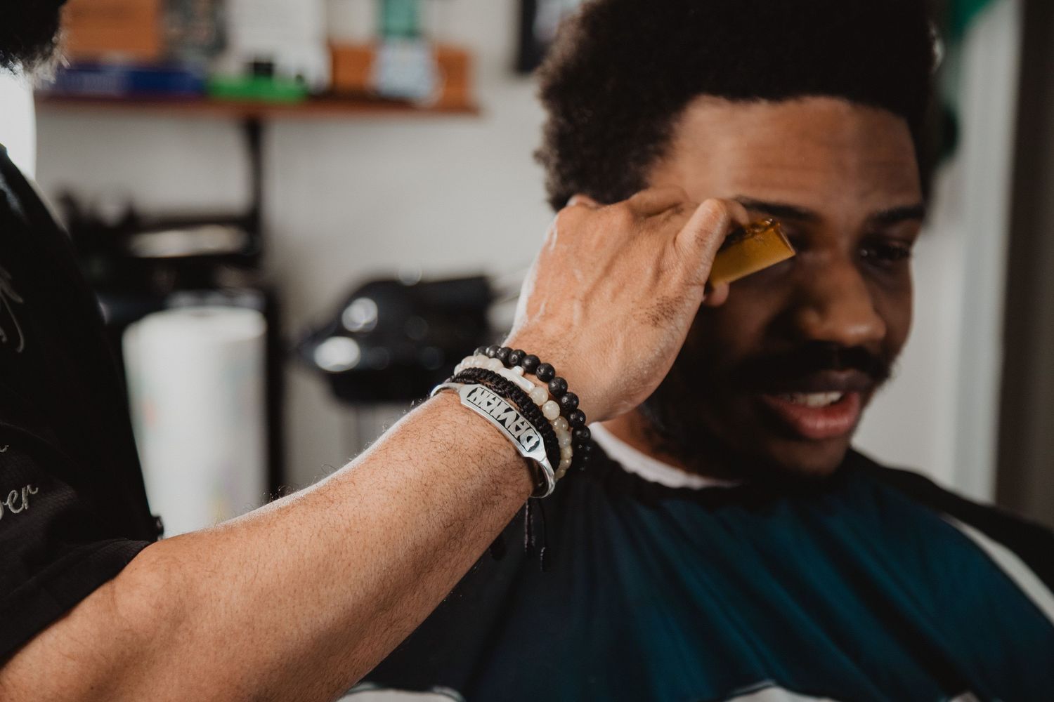 Barber applying a straight razor edge to a young mans hairline during a fresh cut.